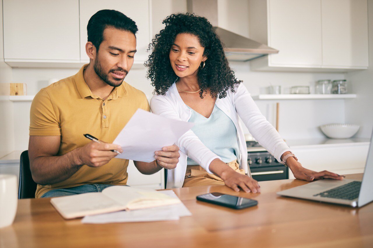 A couple sits at a table in a modern kitchen, reviewing paperwork and researching savings and incentives for using ClimateMaster energy solutions